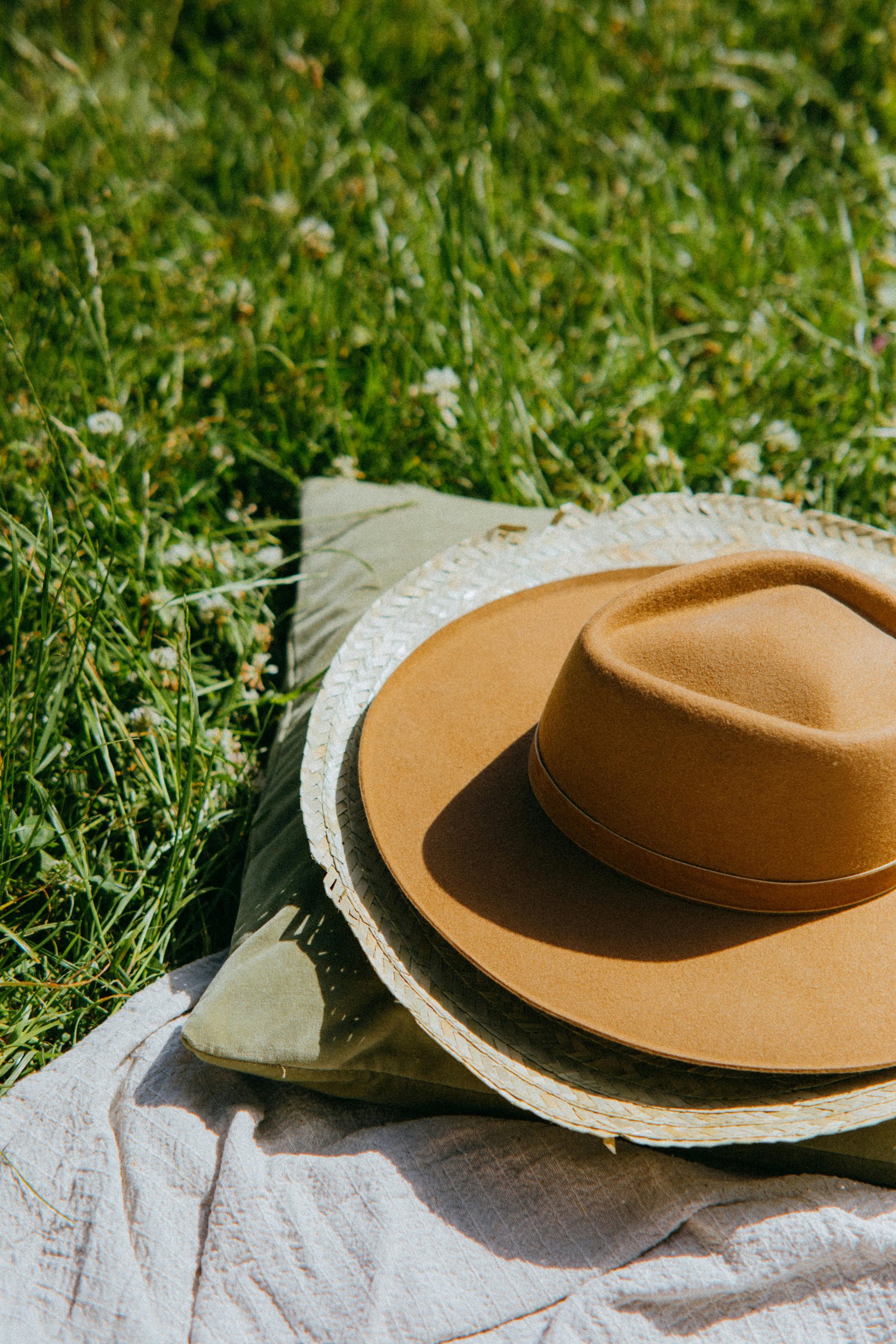 Stylish brown hat on a picnic blanket in sunny grassy field during summer.